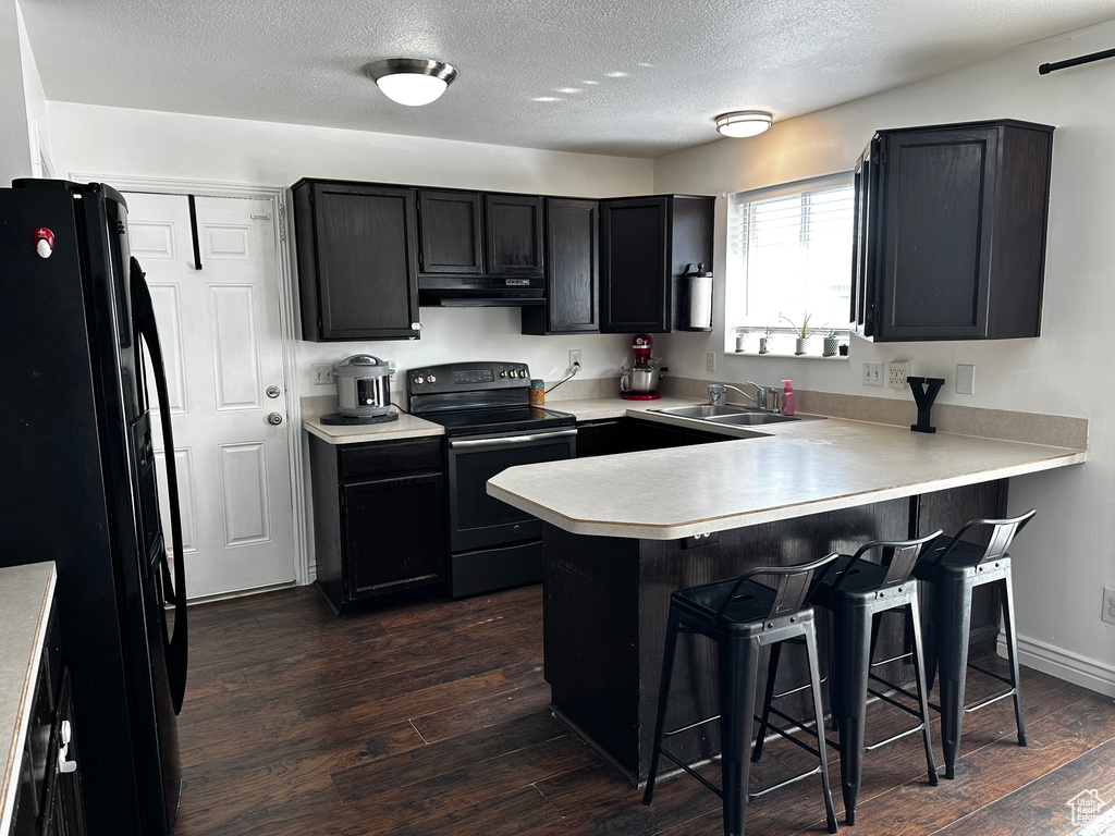 Kitchen featuring black appliances, range hood, a peninsula, a breakfast bar area, and dark cabinetry