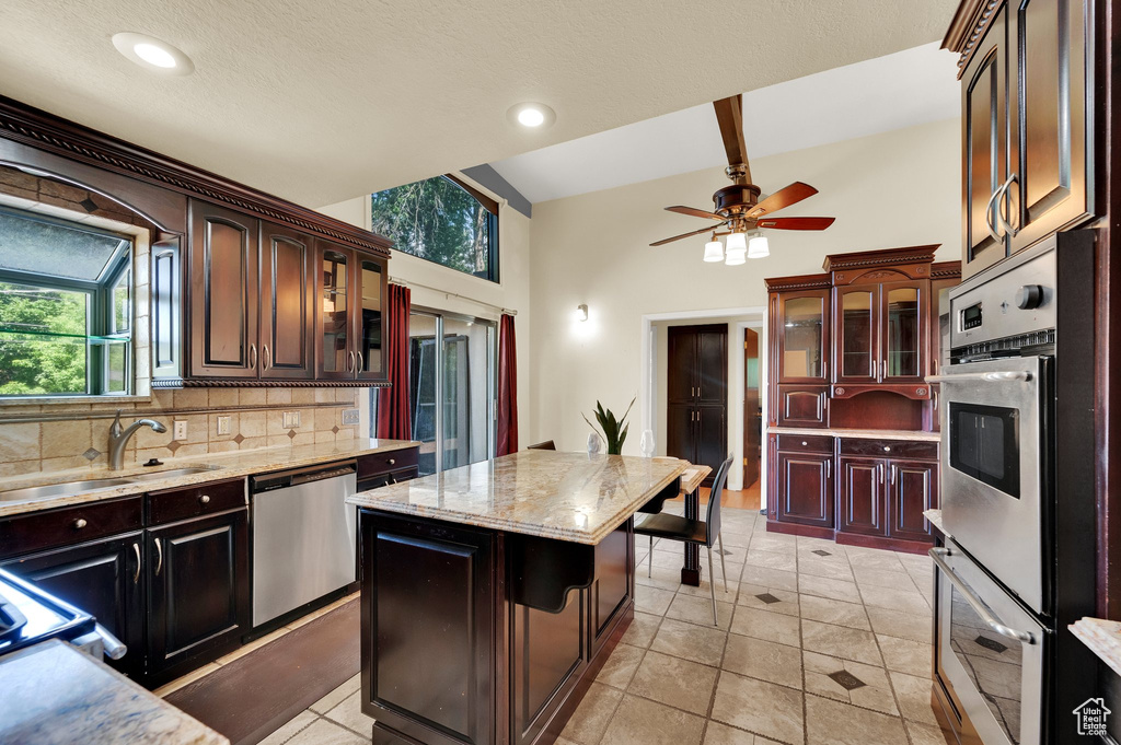 Kitchen with appliances with stainless steel finishes, tasteful backsplash, a kitchen island, glass insert cabinets, and a high ceiling