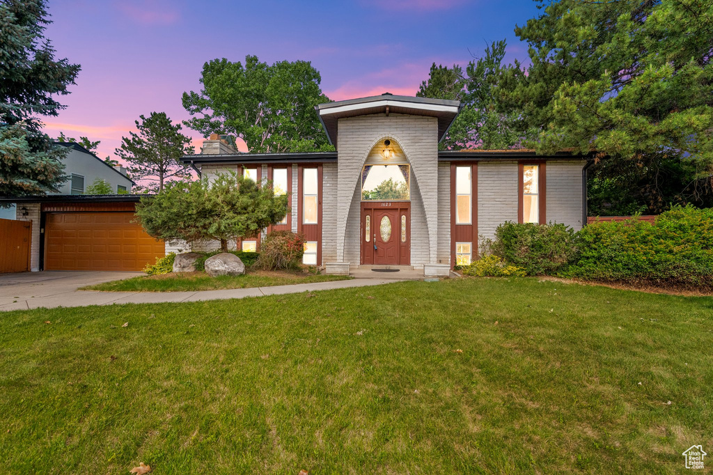 Mid-century home featuring an attached garage, a front lawn, concrete driveway, brick siding, and a chimney