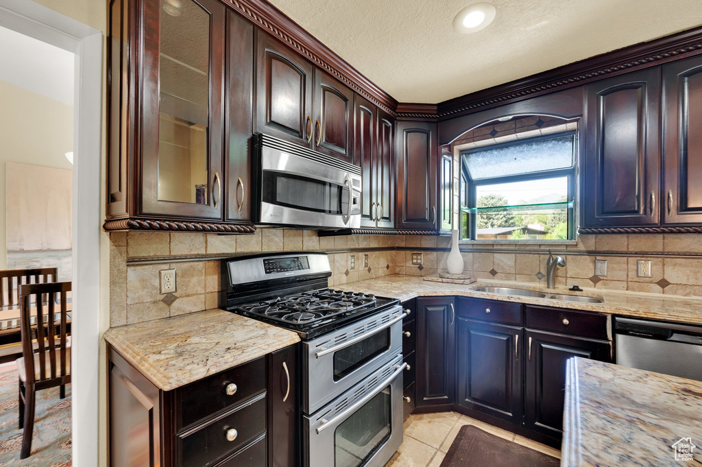 Kitchen with appliances with stainless steel finishes, light stone counters, tasteful backsplash, glass insert cabinets, and a textured ceiling