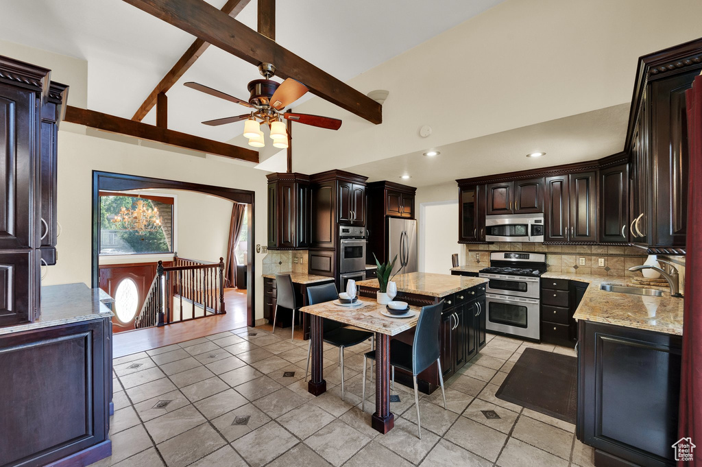 Kitchen with appliances with stainless steel finishes, tasteful backsplash, a ceiling fan, a kitchen island, and light stone counters
