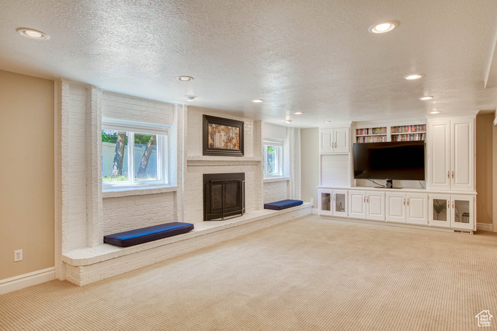 Unfurnished living room featuring light colored carpet, a fireplace, healthy amount of natural light, recessed lighting, and a textured ceiling