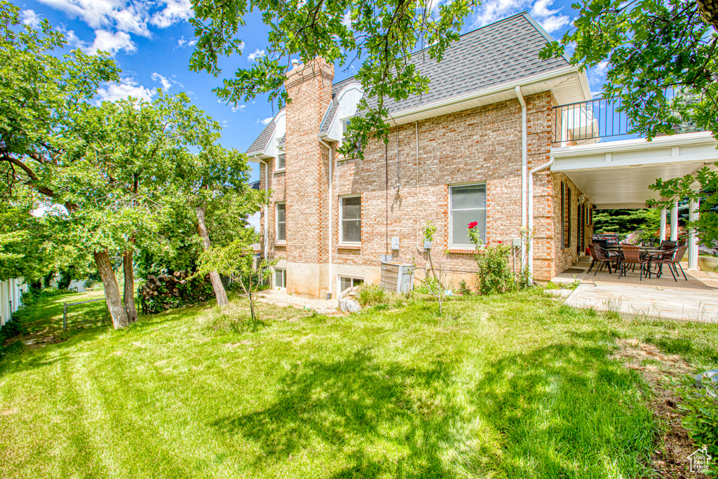 Back of property featuring a balcony, a patio, brick siding, a chimney, and a shingled roof
