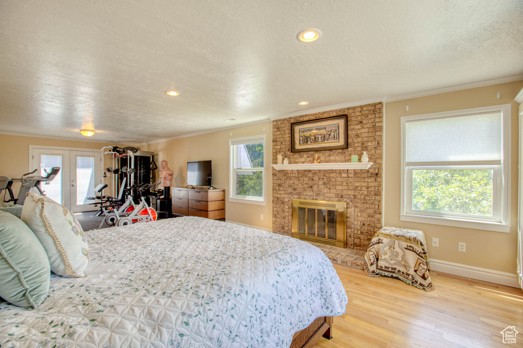 Bedroom with a textured ceiling, ornamental molding, wood finished floors, a brick fireplace, and french doors