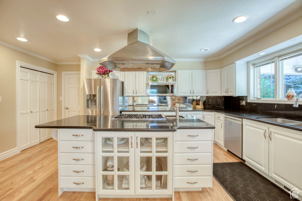 Kitchen featuring appliances with stainless steel finishes, island range hood, dark countertops, crown molding, and white cabinets