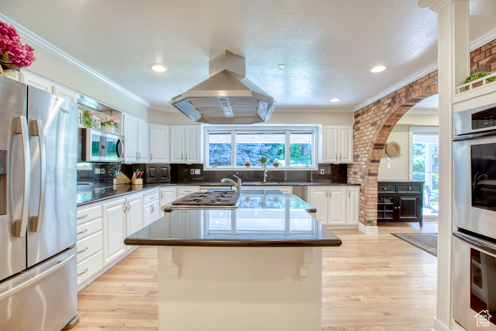 Kitchen featuring stainless steel appliances, island range hood, a center island, white cabinets, and crown molding