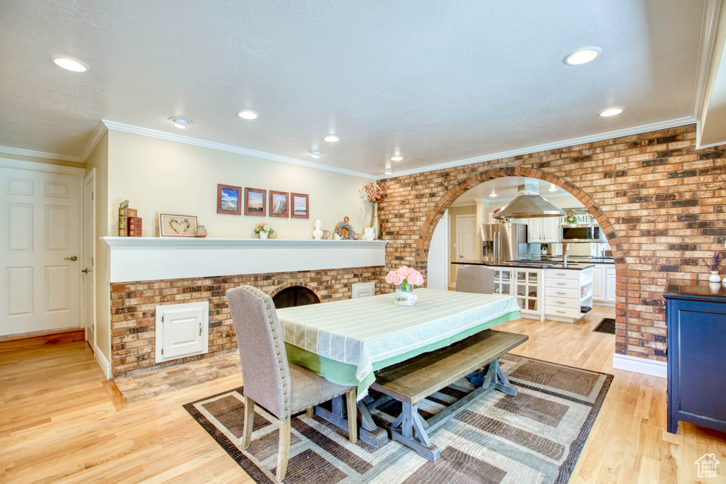 Dining space with arched walkways, light wood finished floors, recessed lighting, ornamental molding, and brick wall
