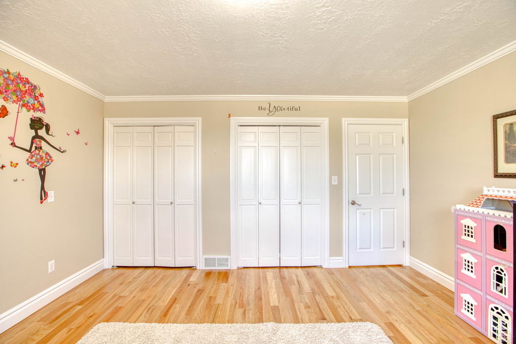 Unfurnished bedroom with two closets, wood finished floors, a textured ceiling, and ornamental molding
