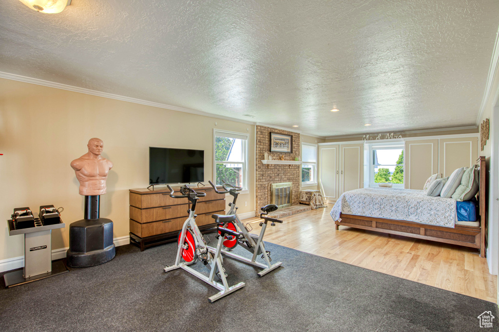 Bedroom featuring a textured ceiling, ornamental molding, wood finished floors, and a brick fireplace