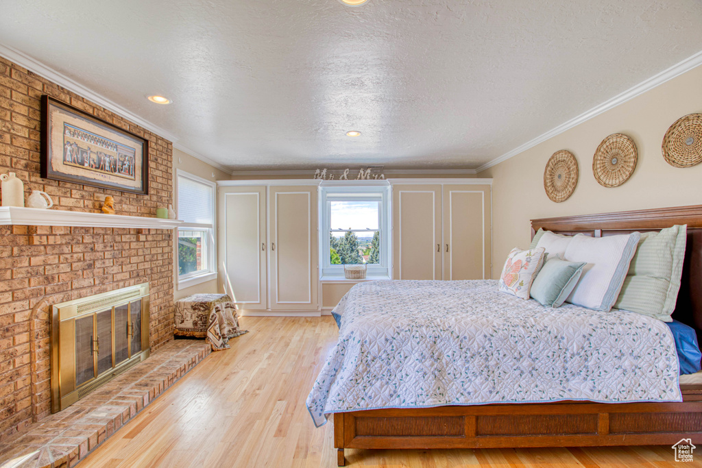Bedroom featuring multiple windows, light wood-style floors, ornamental molding, a brick fireplace, and a textured ceiling