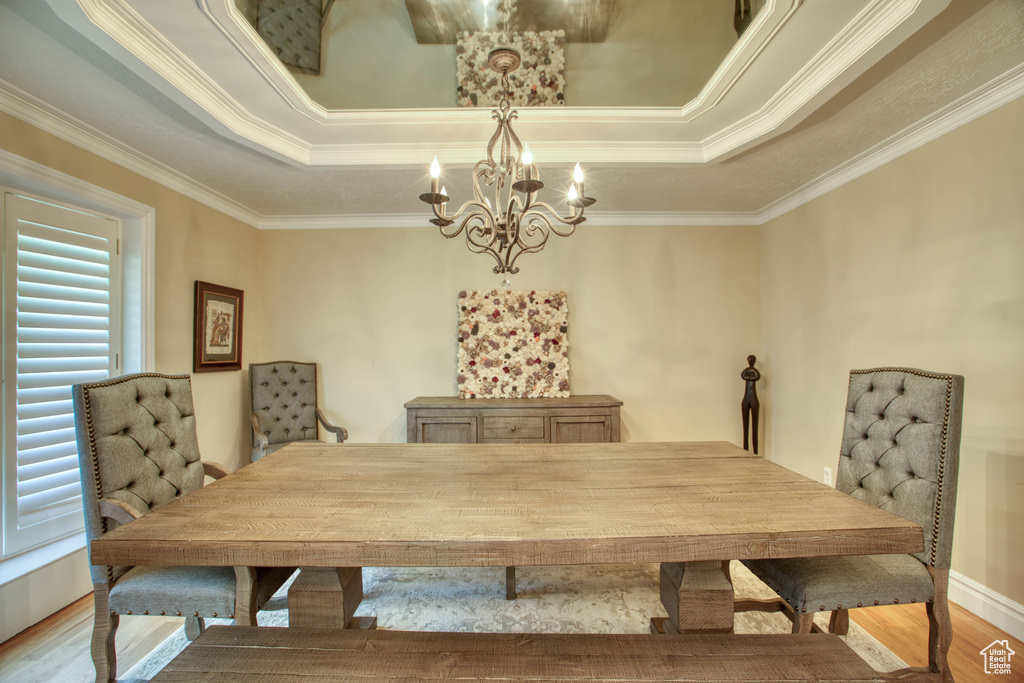 Dining area with a chandelier, a tray ceiling, wood finished floors, and crown molding