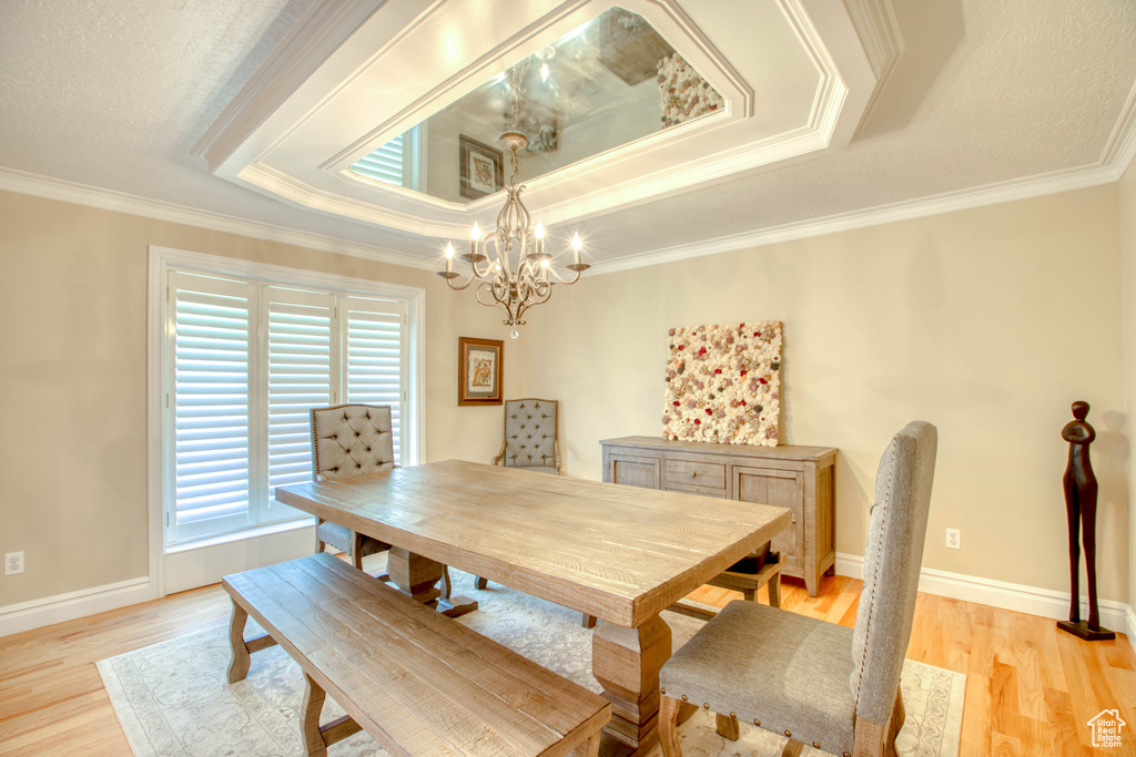 Dining area featuring a raised ceiling, a chandelier, ornamental molding, and light wood-style flooring