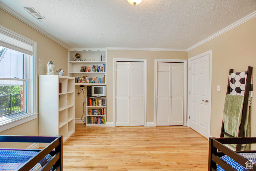 Bedroom with two closets, a textured ceiling, light wood-style flooring, and ornamental molding