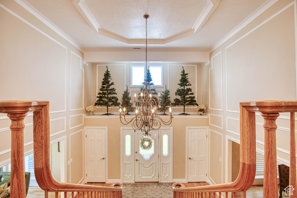 Foyer with a chandelier, a decorative wall, ornamental molding, and a raised ceiling