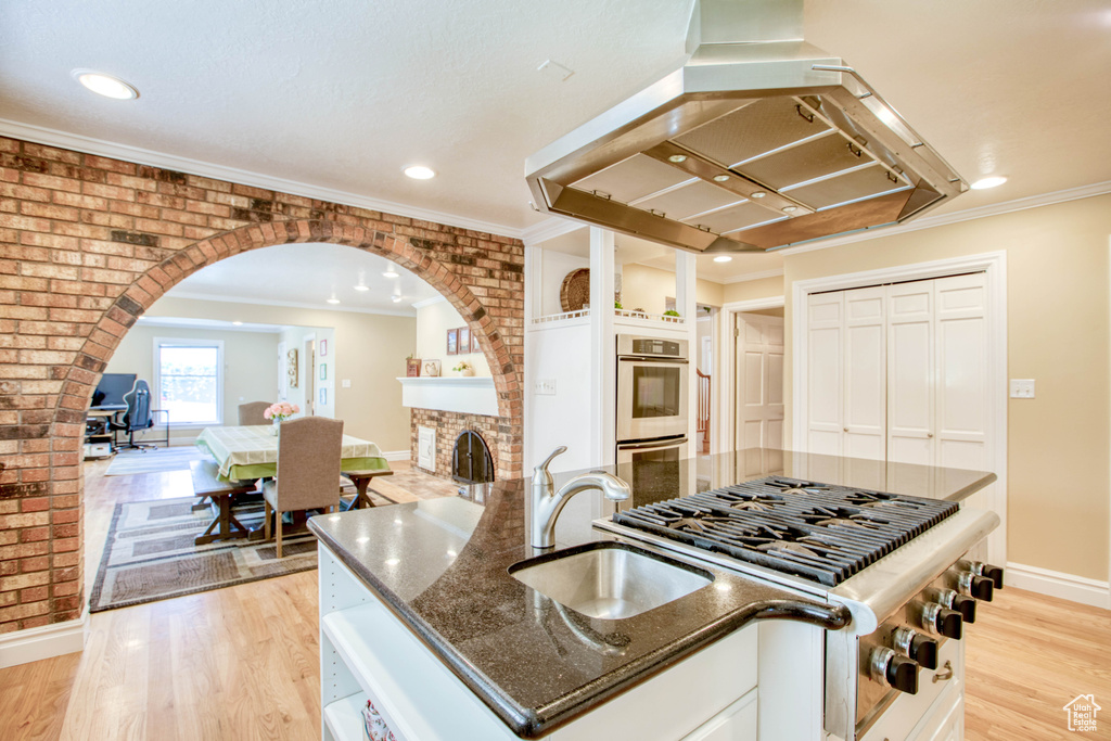 Kitchen with appliances with stainless steel finishes, extractor fan, dark stone countertops, arched walkways, and light wood-style floors