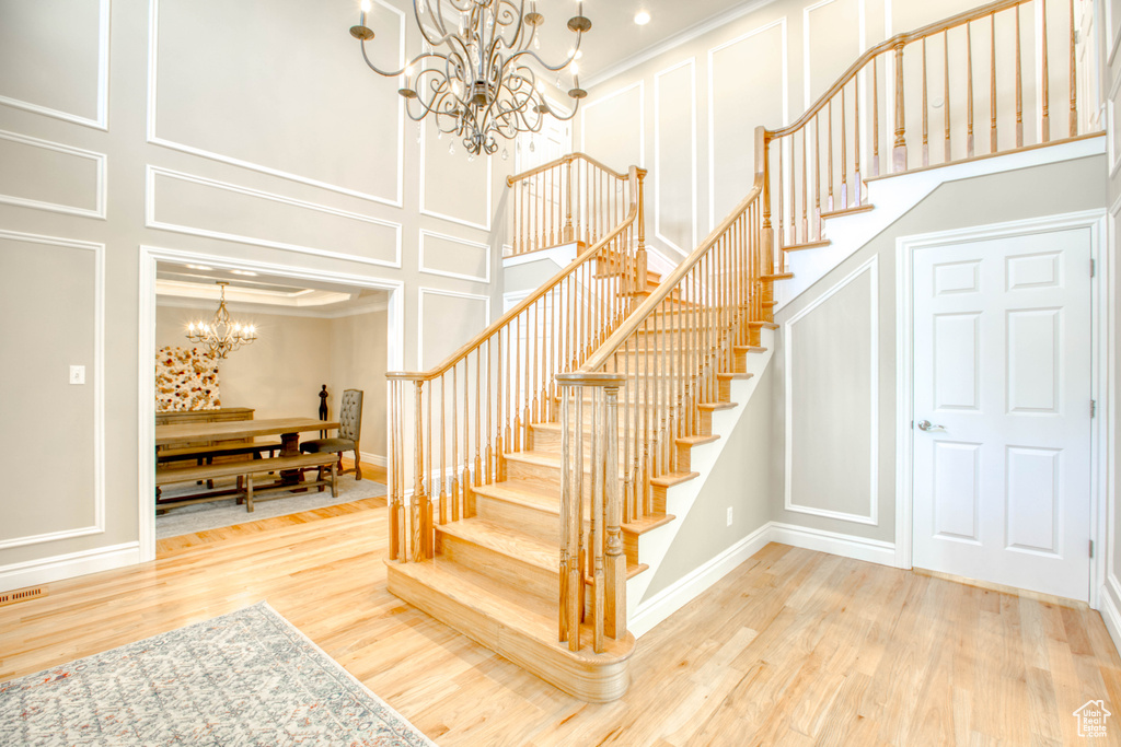 Stairway with a decorative wall, a chandelier, wood finished floors, ornamental molding, and a towering ceiling