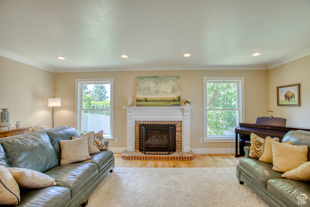 Living room with healthy amount of natural light, light wood finished floors, recessed lighting, a fireplace, and ornamental molding