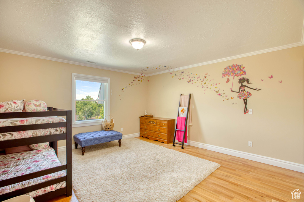 Bedroom with ornamental molding, a textured ceiling, and light wood-style flooring