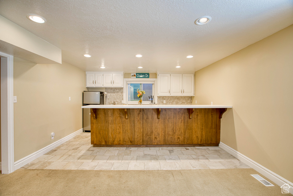 Kitchen featuring a breakfast bar area, fridge, white cabinets, light countertops, and recessed lighting