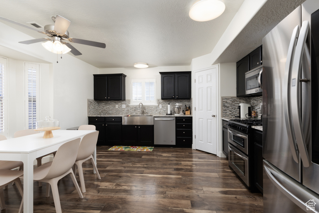 Kitchen with appliances with stainless steel finishes, backsplash, dark wood-style floors, and a ceiling fan