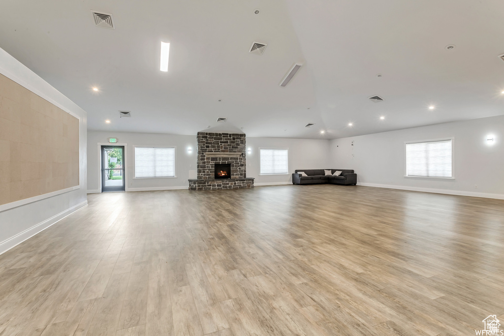 Unfurnished living room featuring light wood-style floors, plenty of natural light, a stone fireplace, and recessed lighting