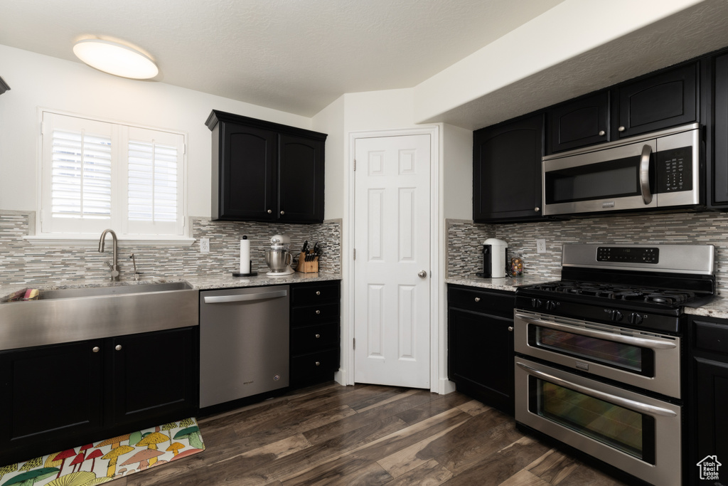 Kitchen featuring stainless steel appliances, dark cabinets, decorative backsplash, and dark wood finished floors