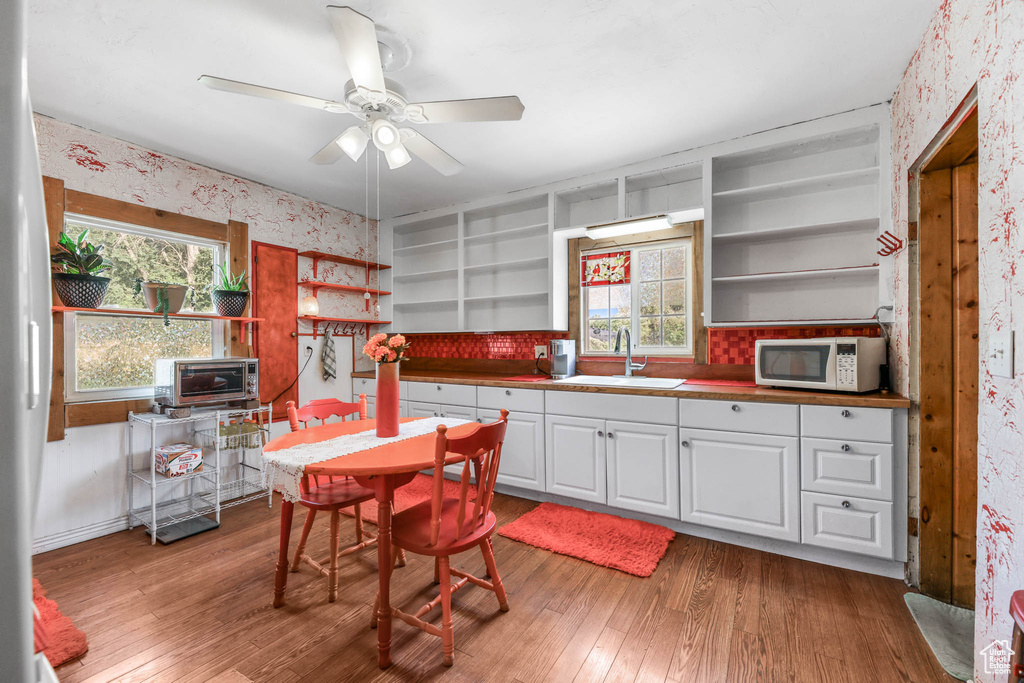 Kitchen with open shelves, wallpapered walls, white appliances, light wood-style floors, and healthy amount of natural light