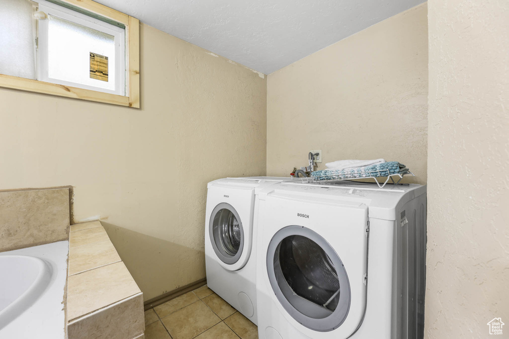 Laundry area with independent washer and dryer and light tile patterned floors