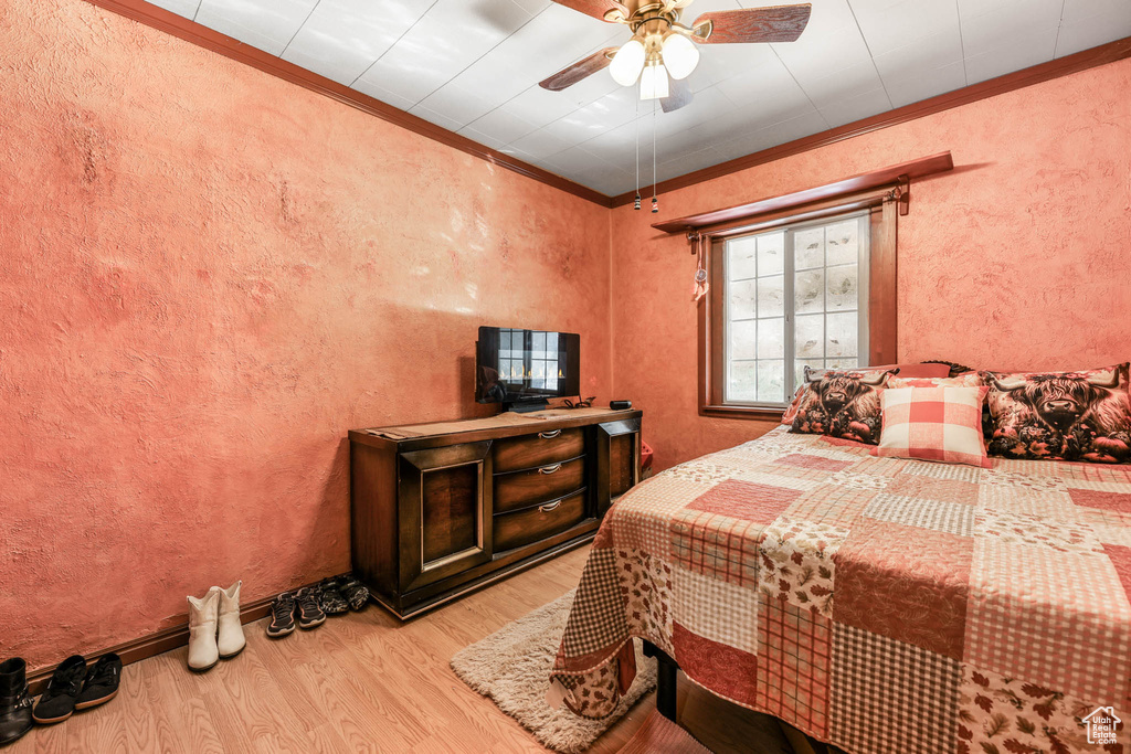Bedroom featuring wood finished floors, crown molding, and a ceiling fan