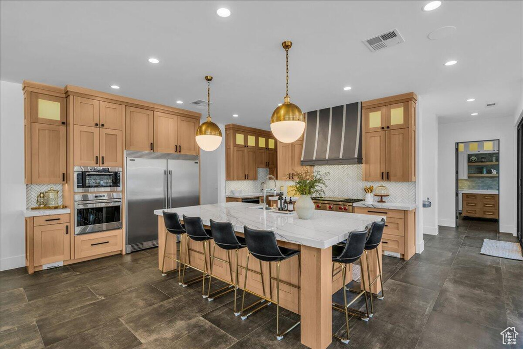 Kitchen featuring stainless steel appliances, wall chimney exhaust hood, backsplash, recessed lighting, and a kitchen island with sink