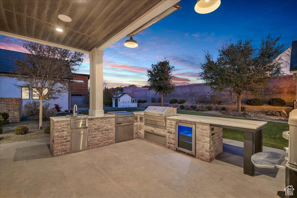 Patio terrace at dusk with exterior kitchen, a patio area, and wine cooler