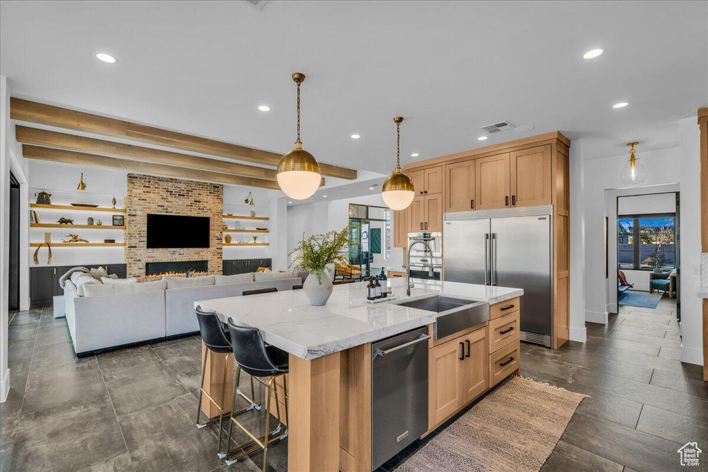 Kitchen with stainless steel appliances, recessed lighting, healthy amount of natural light, light stone counters, and a kitchen island with sink