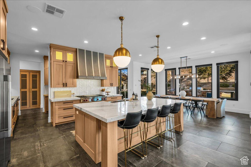 Kitchen featuring exhaust hood, recessed lighting, light stone countertops, backsplash, and glass insert cabinets