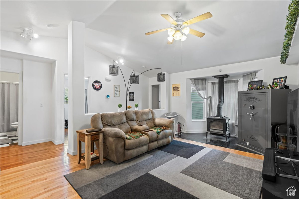 Living area featuring a wood stove, a ceiling fan, light wood finished floors, and vaulted ceiling