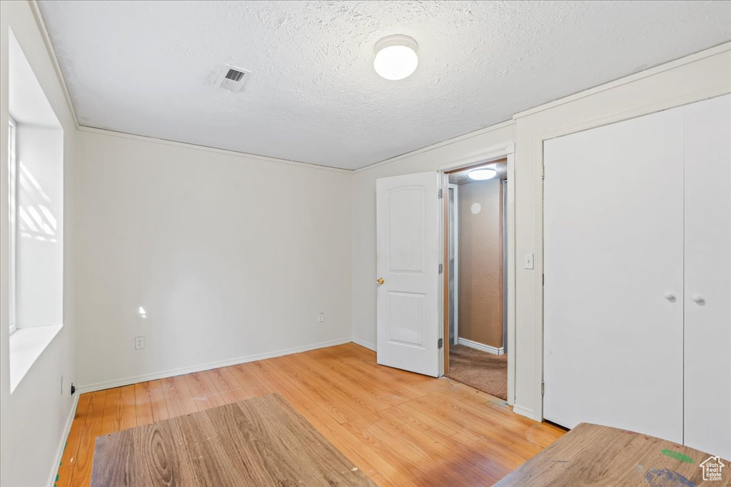 Unfurnished bedroom featuring light wood-type flooring, a closet, and a textured ceiling