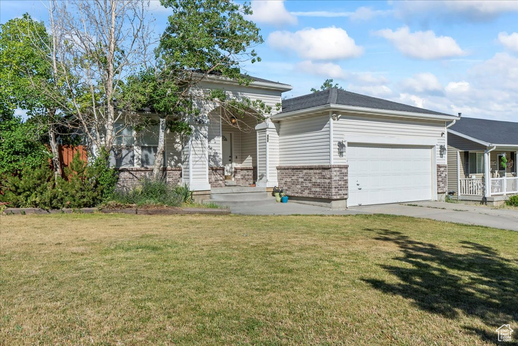 View of front of property with a garage, a porch, a front yard, concrete driveway, and brick siding