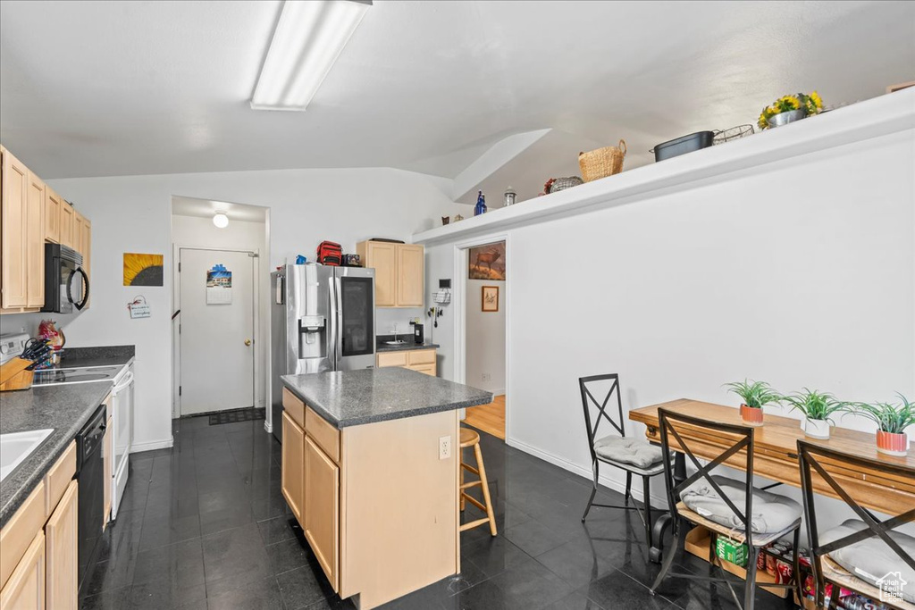 Kitchen with black appliances, lofted ceiling, light brown cabinetry, dark countertops, and a center island