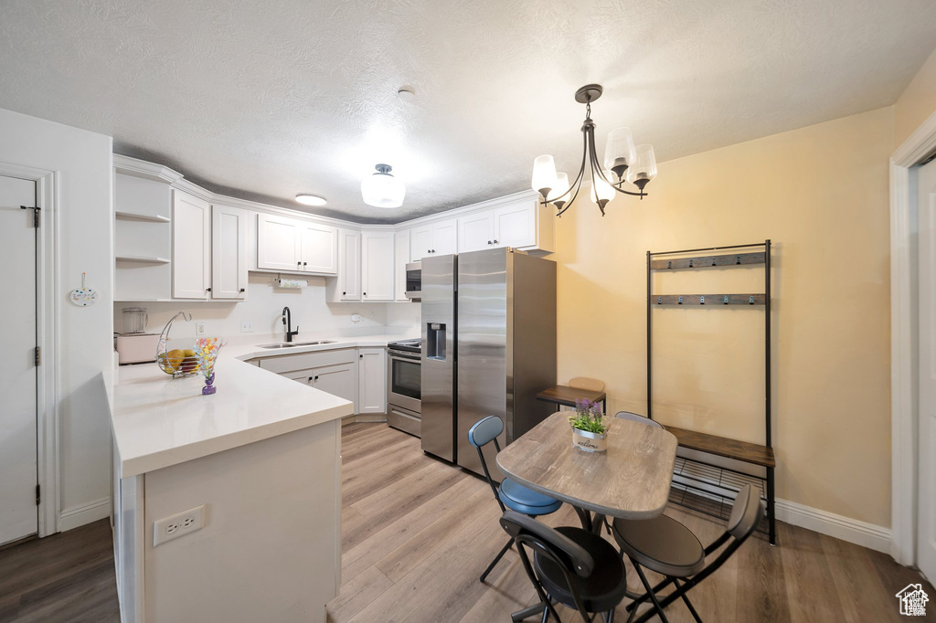 Kitchen with stainless steel appliances, white cabinetry, light countertops, and light wood-style floors