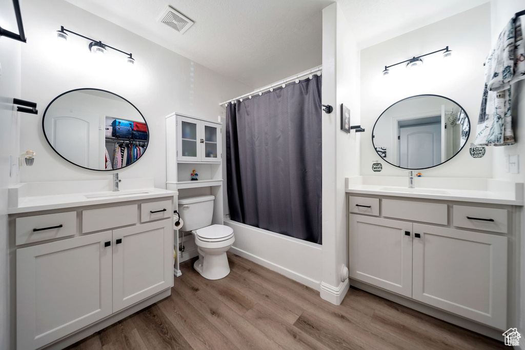 Bathroom with wood finished floors, vanity, and shower / tub combo with curtain