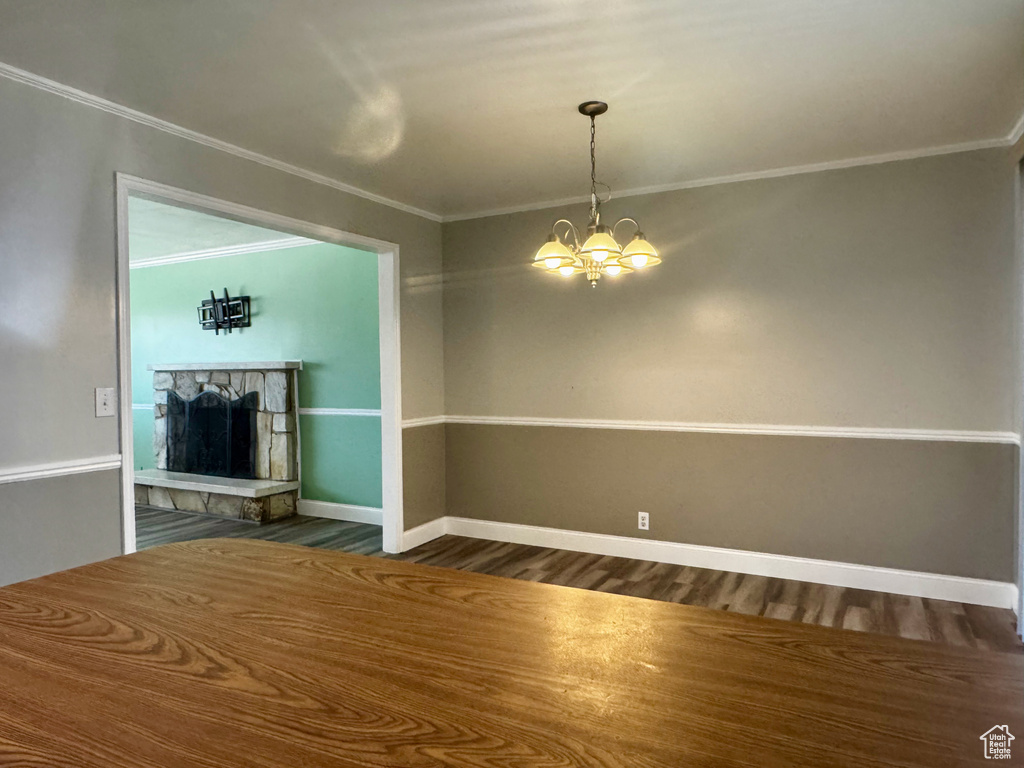 Unfurnished living room featuring crown molding, dark wood-type flooring, a stone fireplace, and a chandelier
