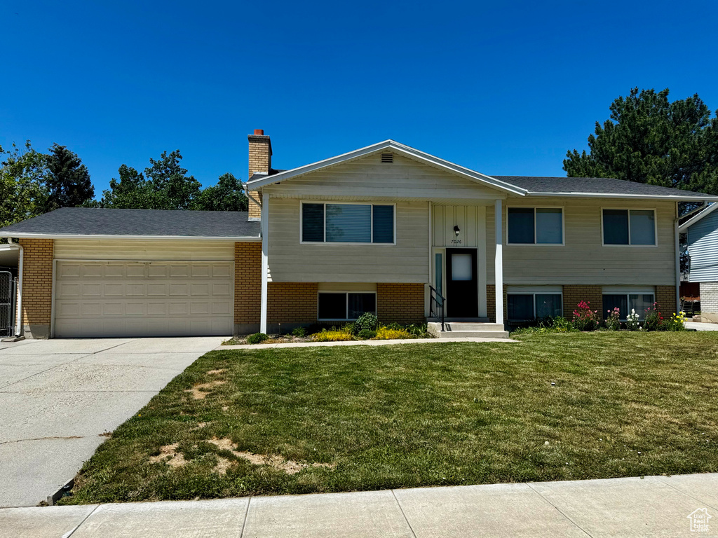 Bi-level home with an attached garage, brick siding, a chimney, driveway, and a front yard