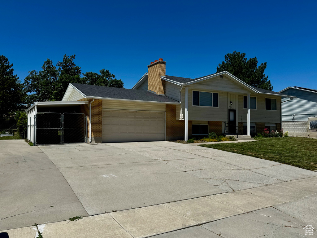 Bi-level home with brick siding, a garage, concrete driveway, a chimney, and a front yard