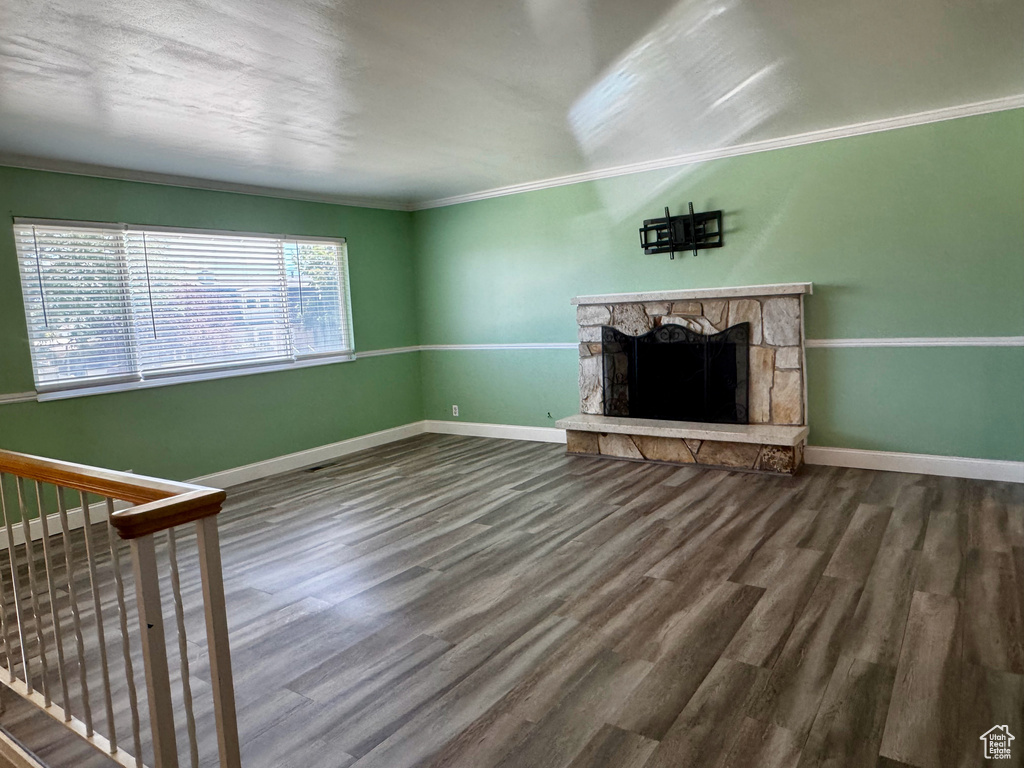 Unfurnished living room featuring crown molding, wood finished floors, and a stone fireplace