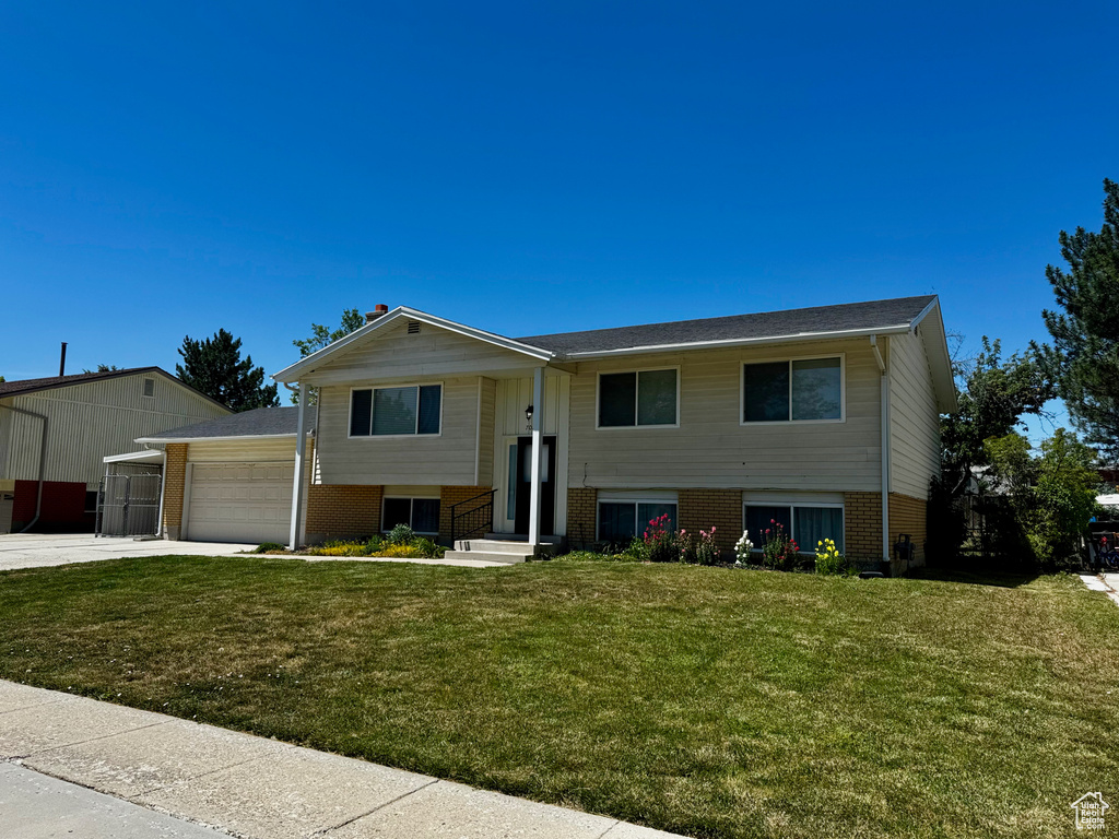 Bi-level home with brick siding, an attached garage, a front yard, and concrete driveway