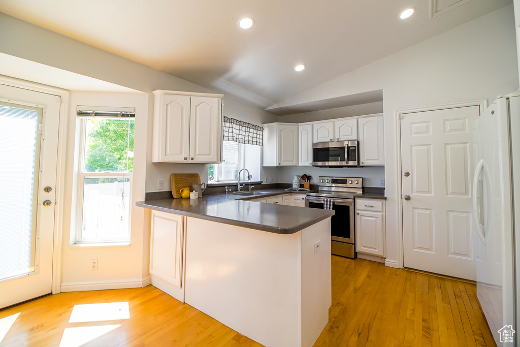 Kitchen with stainless steel appliances, dark countertops, a peninsula, white cabinetry, and lofted ceiling