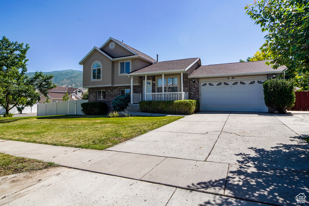 Tri-level home with a garage, brick siding, concrete driveway, covered porch, and a mountain view