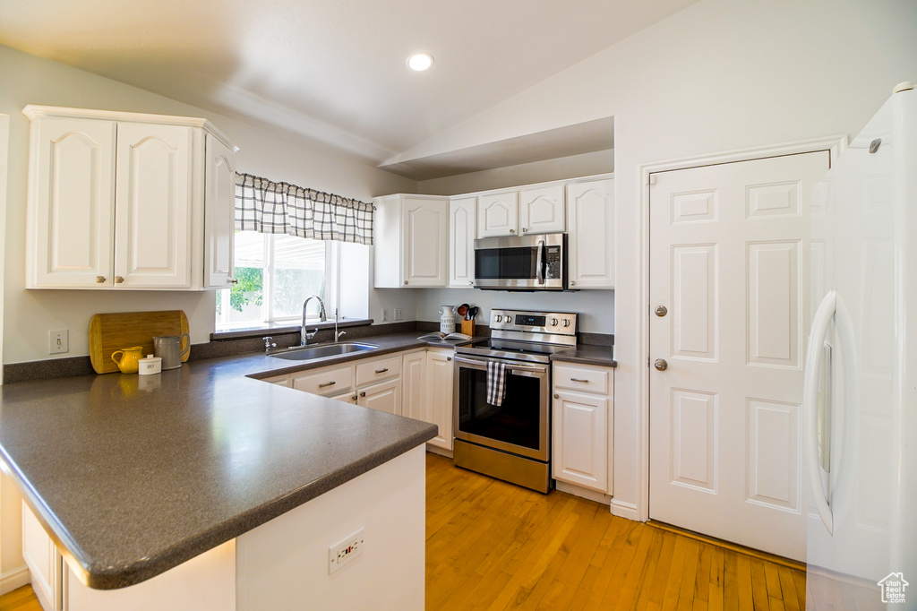 Kitchen featuring appliances with stainless steel finishes, dark countertops, a peninsula, lofted ceiling, and white cabinets