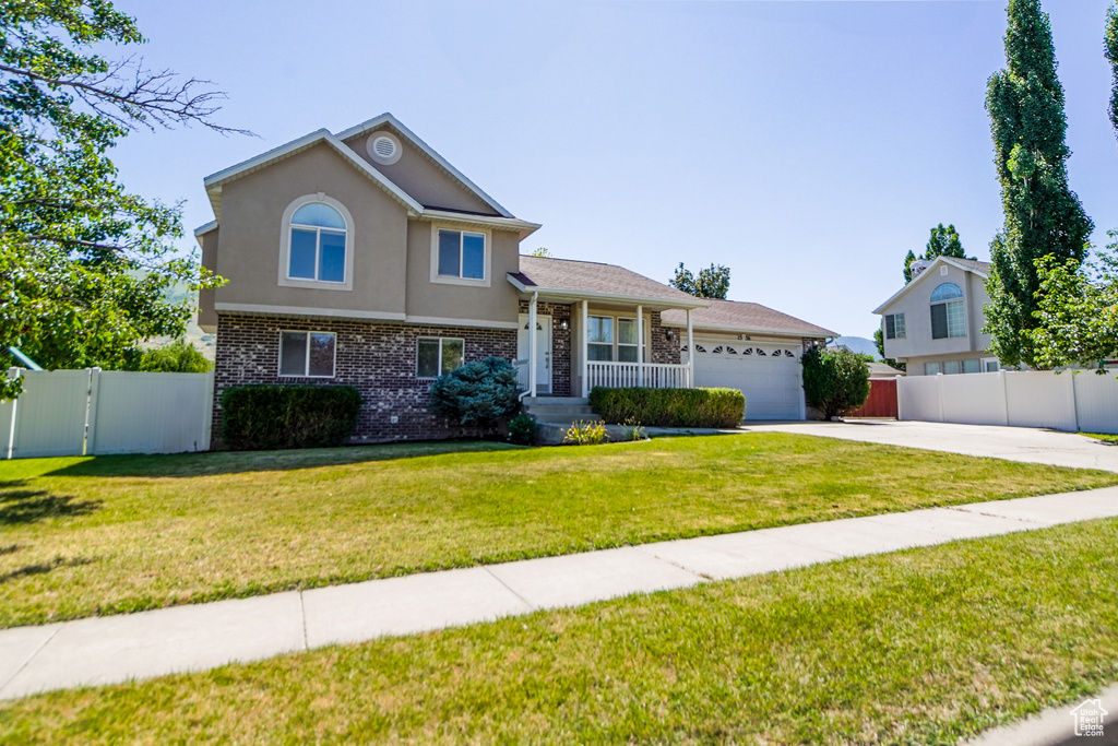 Split level home featuring an attached garage, brick siding, concrete driveway, stucco siding, and a gate