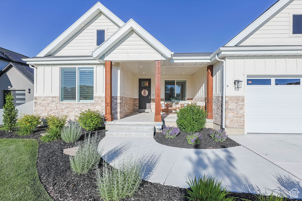 Property entrance with stone siding, board and batten siding, a porch, and a garage
