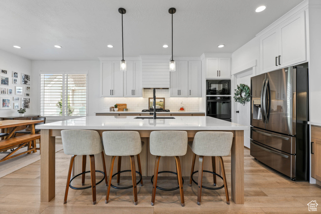 Kitchen featuring black appliances, light countertops, a breakfast bar, decorative backsplash, and recessed lighting